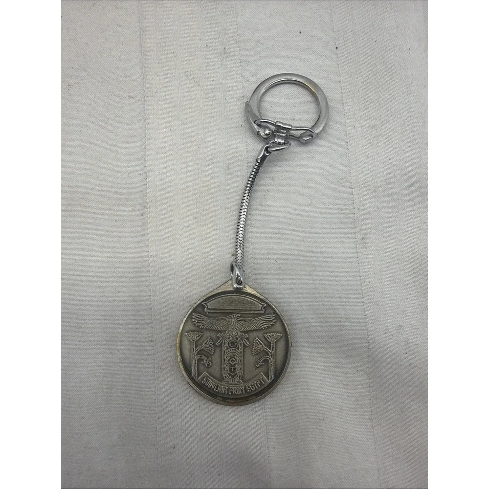 silver-toned keychain with a round charm featuring a‎ detailed relief scene